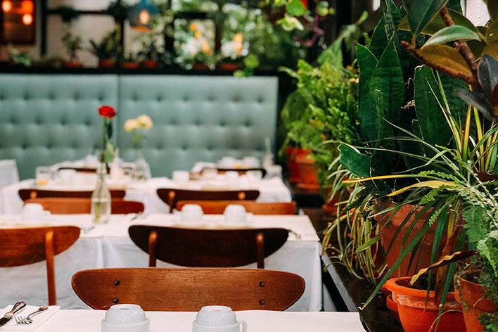A restaurant with tables and chairs, potted plants.