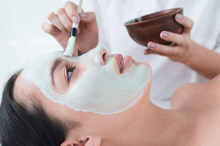 A woman getting her face painted with a white mask.