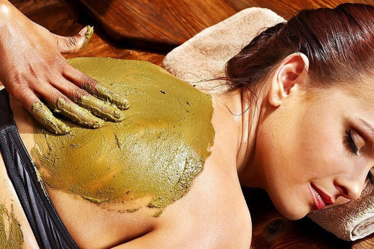 A woman is getting her back covered in mud.