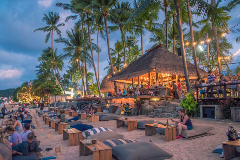 A beach with people sitting on benches and tables